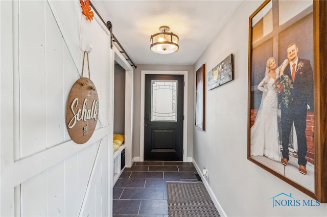 doorway featuring baseboards, a barn door, and dark tile patterned flooring
