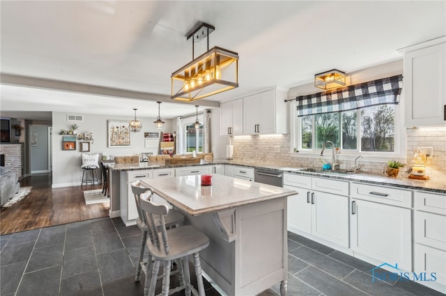 kitchen featuring stainless steel dishwasher, a sink, a peninsula, and light stone countertops