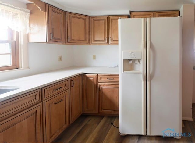 kitchen with light countertops, dark wood-style flooring, brown cabinetry, and white fridge with ice dispenser