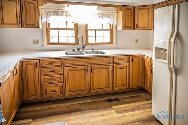 kitchen featuring a sink, light countertops, brown cabinetry, white fridge with ice dispenser, and visible vents