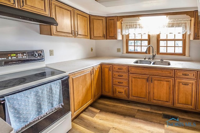 kitchen featuring visible vents, brown cabinetry, under cabinet range hood, a sink, and range with electric cooktop