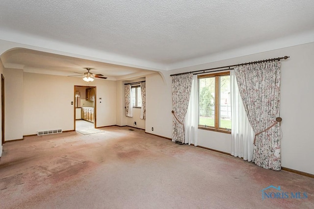 empty room featuring visible vents, light carpet, baseboards, ceiling fan, and arched walkways