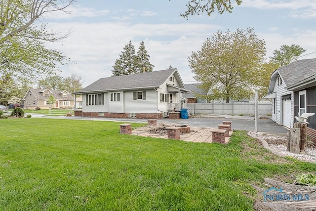 back of property with fence, a shingled roof, a lawn, a patio, and a fire pit