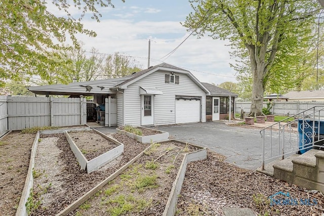 view of front of house with an attached garage, a garden, a fenced backyard, and aphalt driveway