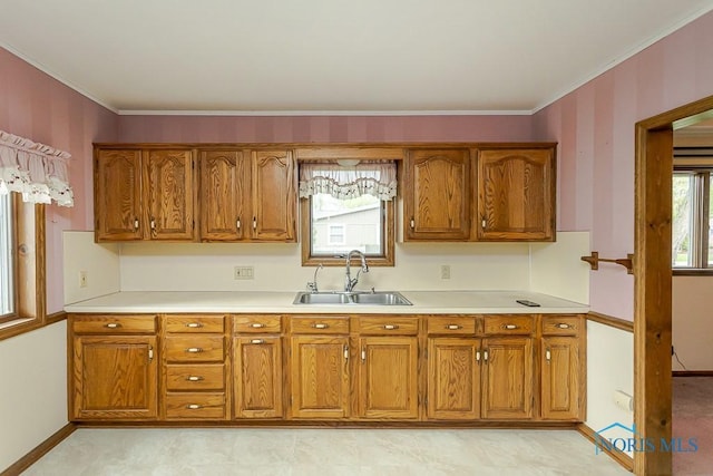 kitchen with ornamental molding, baseboards, light countertops, brown cabinets, and a sink