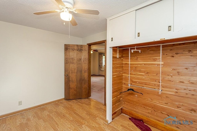 interior space featuring light wood-style floors, baseboards, a ceiling fan, and a textured ceiling
