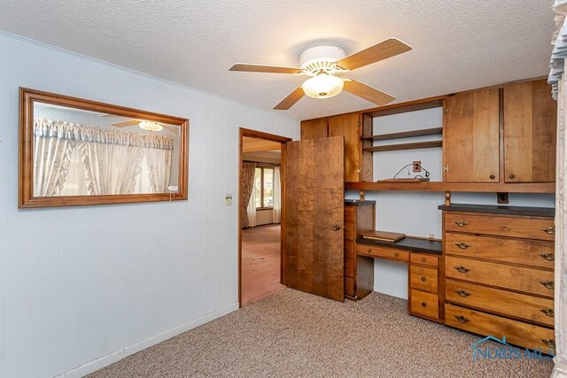 unfurnished office featuring a textured ceiling, ceiling fan, light colored carpet, and built in study area