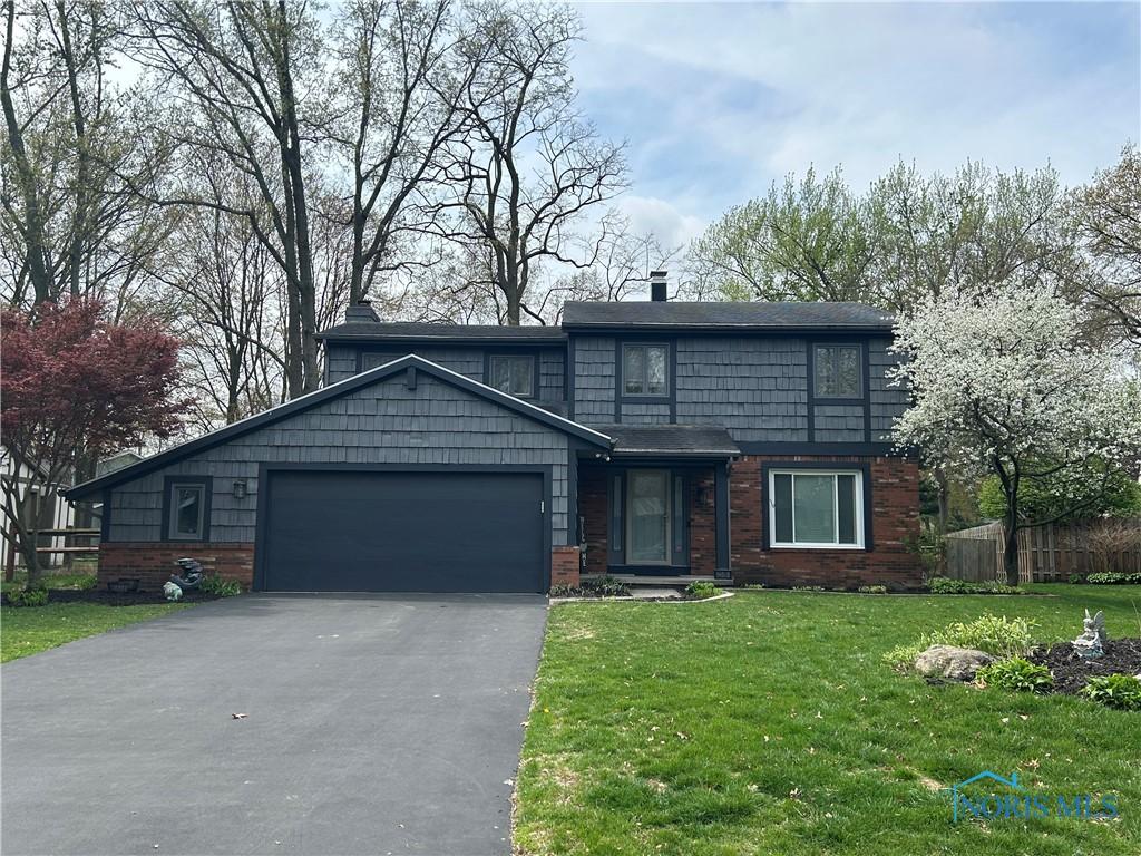 traditional-style home with fence, an attached garage, brick siding, a front yard, and driveway