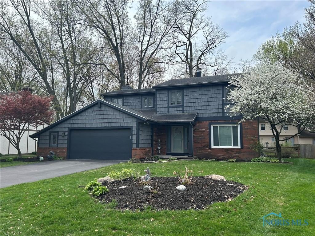 traditional-style house with an attached garage, driveway, a front lawn, and brick siding