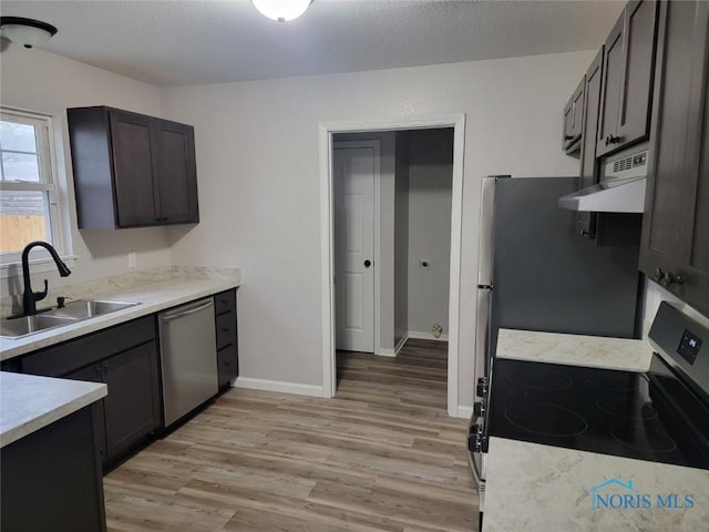 kitchen with appliances with stainless steel finishes, a sink, light wood-style floors, light countertops, and extractor fan