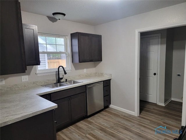 kitchen featuring baseboards, light wood-type flooring, light countertops, a sink, and dishwasher