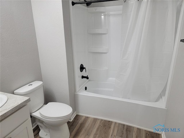 full bath featuring vanity, shower / bath combo with shower curtain, a textured wall, wood finished floors, and toilet