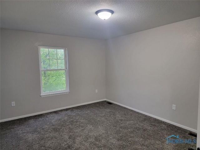 spare room with a textured ceiling, baseboards, and dark colored carpet