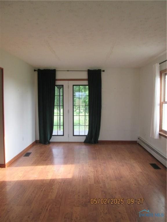 spare room with french doors, visible vents, baseboard heating, wood finished floors, and baseboards