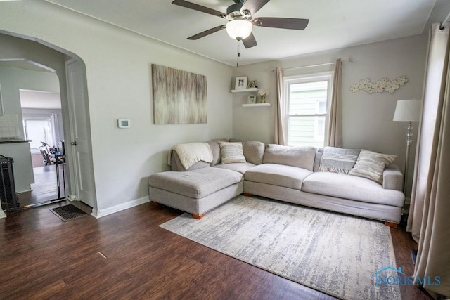 living area featuring baseboards, ceiling fan, arched walkways, and wood finished floors