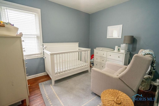 bedroom with baseboards, a crib, and wood finished floors