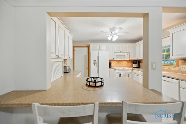 kitchen with ceiling fan, a kitchen bar, tasteful backsplash, a peninsula, and white appliances