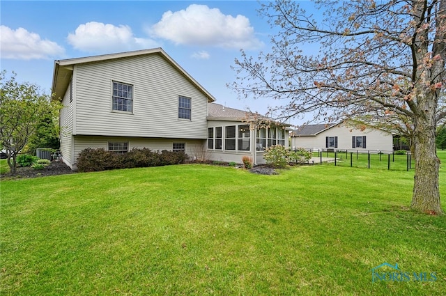 rear view of house with a sunroom, a lawn, and fence