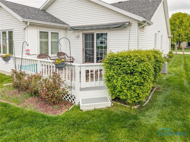 rear view of property with a yard, a deck, and a shingled roof