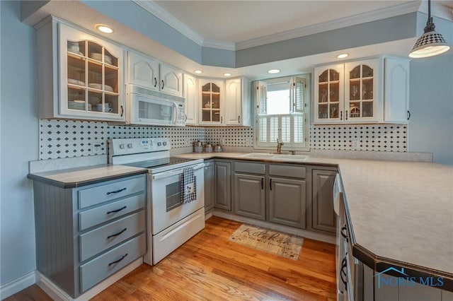 kitchen with crown molding, a sink, white appliances, light countertops, and decorative backsplash