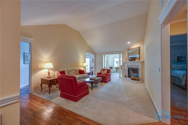 living area with baseboards, wood finished floors, lofted ceiling, and a high end fireplace