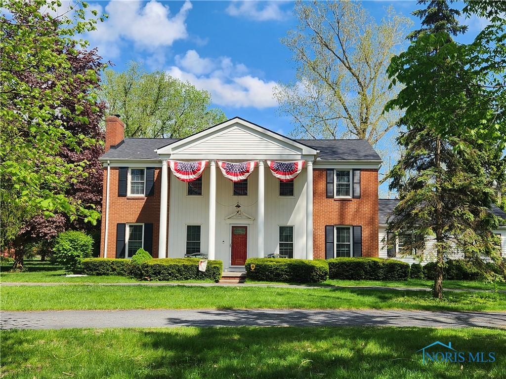 greek revival house with a chimney, a front yard, and brick siding