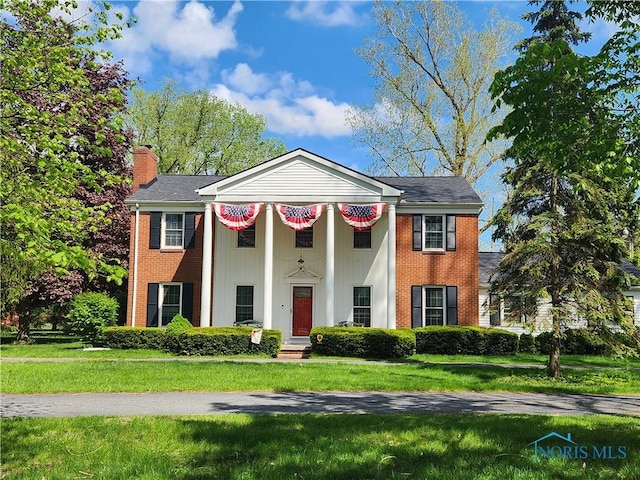 greek revival house with a chimney, a front yard, and brick siding