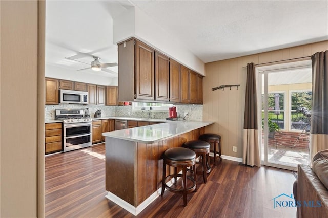 106 N Munson Rd, Swanton, OH 43558 - kitchen featuring appliances with stainless steel finishes, dark wood finished floors, backsplash, a peninsula, and a breakfast bar area