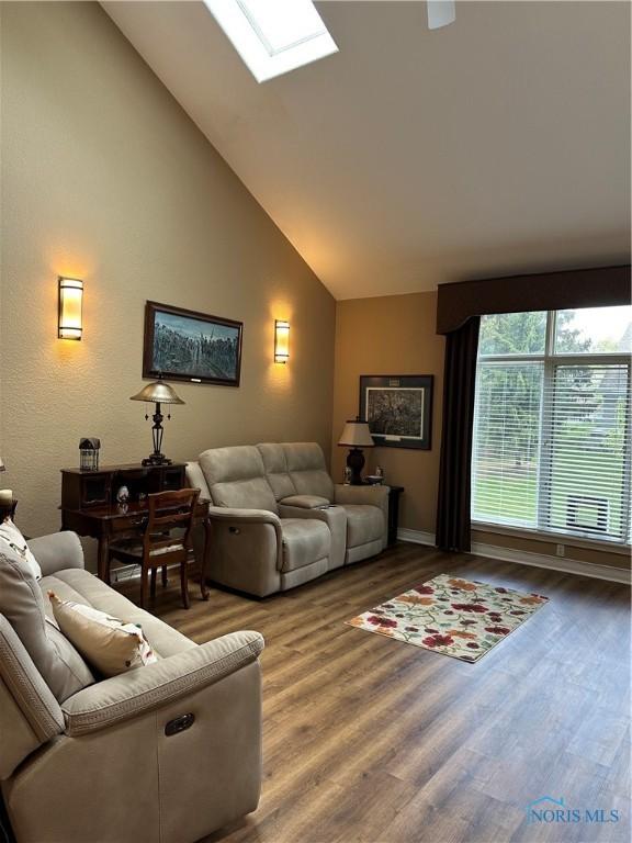 living area featuring baseboards, a skylight, wood finished floors, and high vaulted ceiling