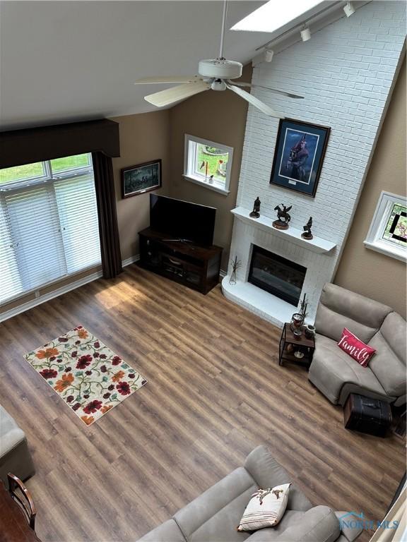 living room with a ceiling fan, a healthy amount of sunlight, vaulted ceiling with skylight, and wood finished floors