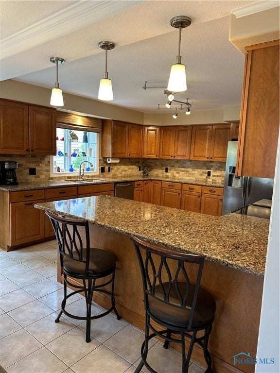 kitchen featuring appliances with stainless steel finishes, a breakfast bar, a sink, brown cabinetry, and stone counters
