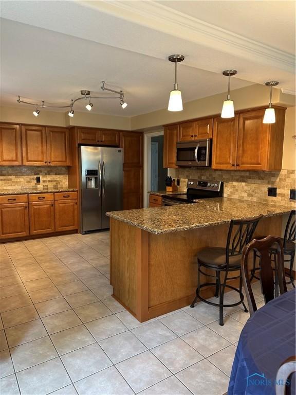 kitchen featuring decorative backsplash, stainless steel appliances, brown cabinetry, and a peninsula