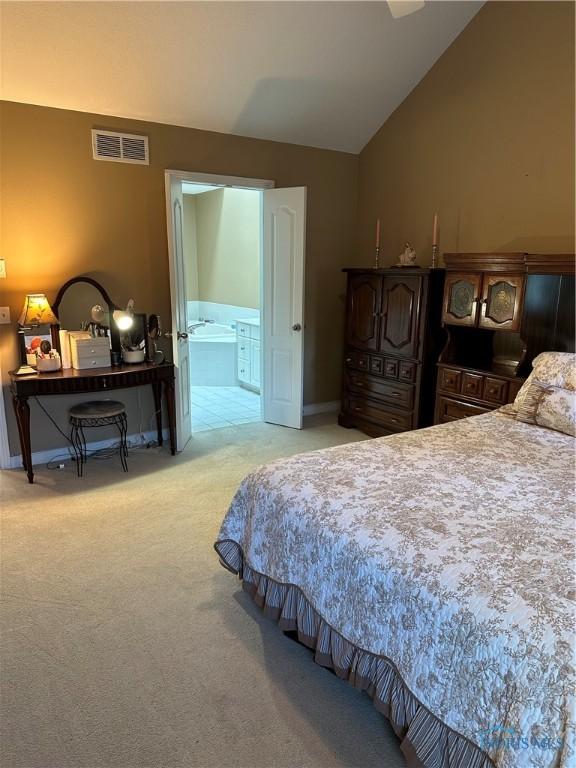 bedroom with visible vents, baseboards, lofted ceiling, light carpet, and ensuite bath