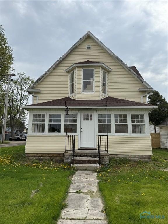 bungalow-style house featuring entry steps, a shingled roof, and a front lawn