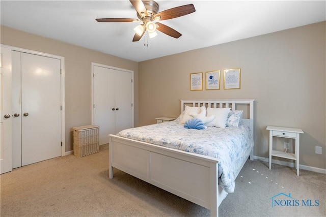 bedroom with light colored carpet, ceiling fan, multiple closets, and baseboards