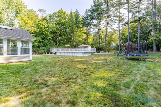 view of yard featuring a swimming pool, a playground, and a trampoline