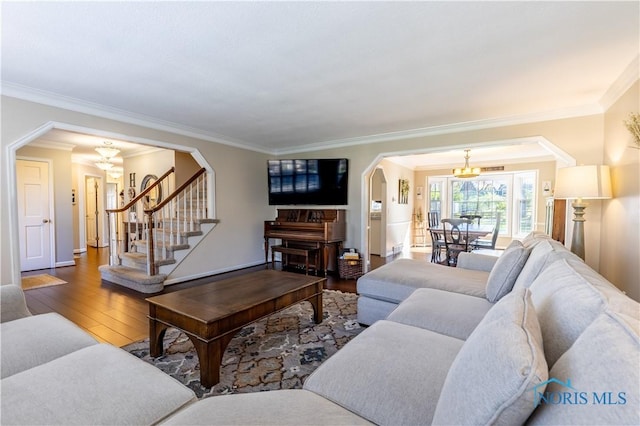 living room featuring crown molding, arched walkways, a chandelier, stairs, and wood finished floors