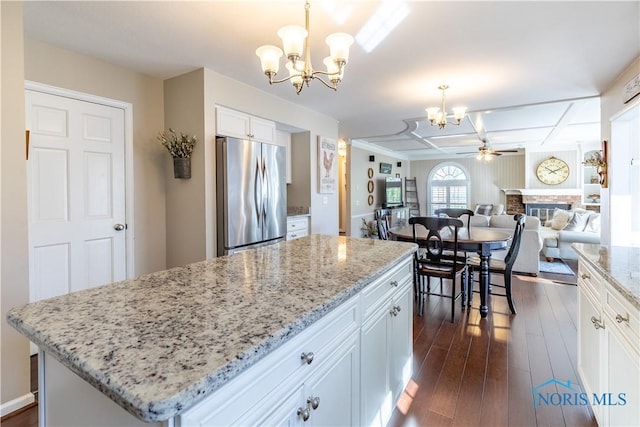 kitchen with stainless steel refrigerator, a fireplace, dark wood-style floors, white cabinets, and ceiling fan with notable chandelier