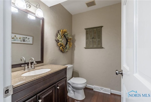 half bath featuring visible vents, wood finished floors, toilet, and vanity