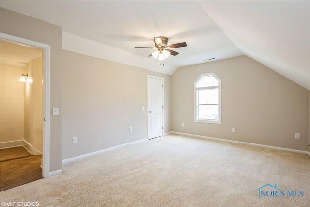 interior space with baseboards, ceiling fan, vaulted ceiling, and light carpet