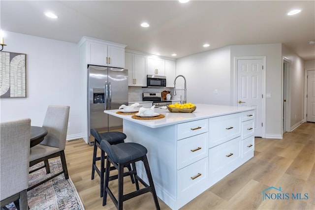 26328 Stillwater Dr, Perrysburg, OH 43551 - kitchen featuring appliances with stainless steel finishes, light wood-style flooring, a breakfast bar, white cabinetry, and light countertops