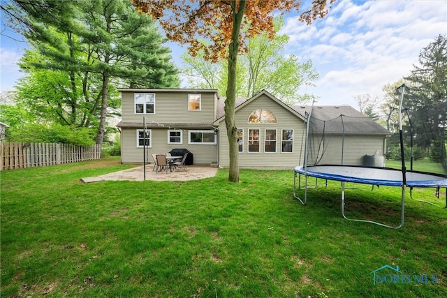 rear view of house featuring fence, a trampoline, a yard, and a patio