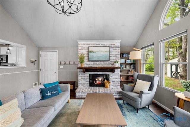 living room with a notable chandelier, a fireplace, high vaulted ceiling, wood finished floors, and visible vents