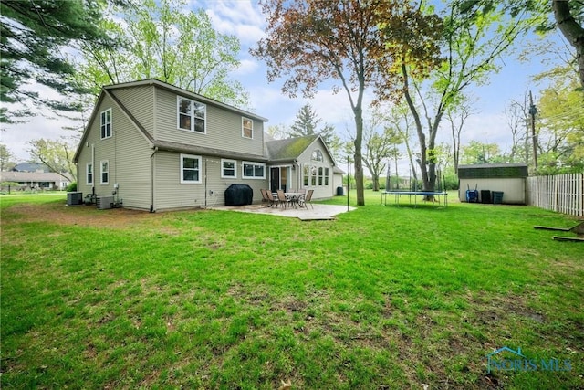 rear view of property with an outdoor structure, a patio, a storage unit, a trampoline, and a yard