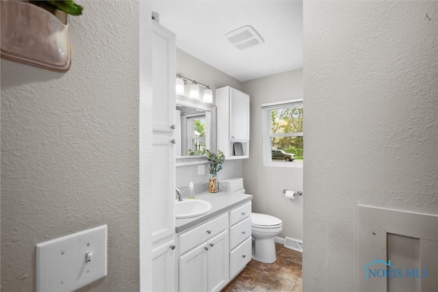 bathroom with a textured wall, toilet, and visible vents