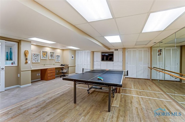 game room featuring light wood-style floors, baseboards, built in desk, and a drop ceiling