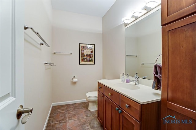 bathroom with toilet, baseboards, stone finish floor, and vanity