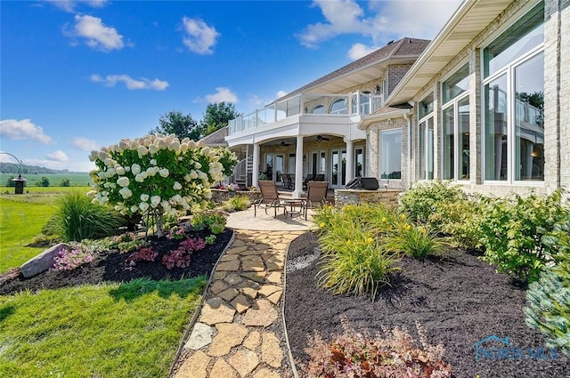 back of property featuring brick siding, a ceiling fan, a patio area, and a balcony