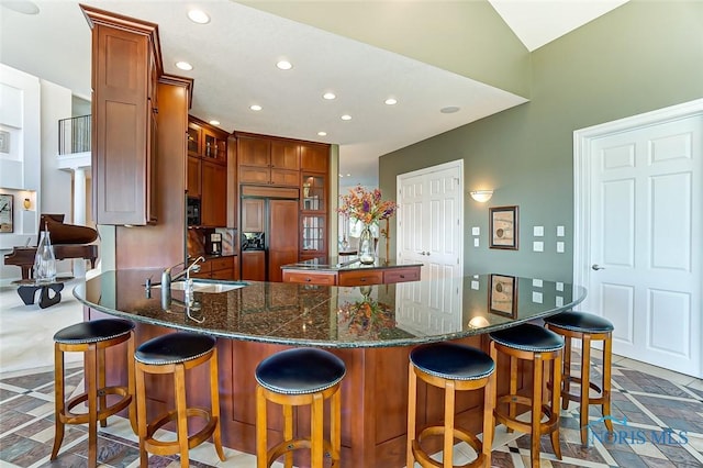 kitchen with brown cabinetry, a sink, paneled built in refrigerator, glass insert cabinets, and recessed lighting