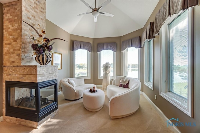 living area featuring a ceiling fan, a fireplace, baseboards, high vaulted ceiling, and carpet flooring